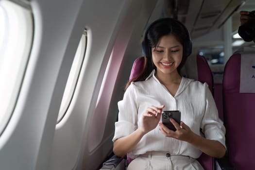 Asian business woman on aeroplane using smartphone.