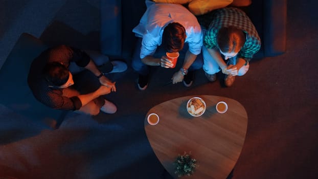 Family and colleague sitting at dark living room with red filter while cheering football team together. Caucasian people enjoy watching tv and giving high five to celebrate winning team. Convocation.