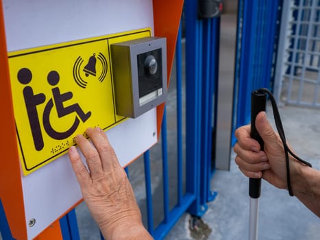 Close-up of the hands of a blind elderly woman reading a text in braille. Button for calling help for people with disabilities