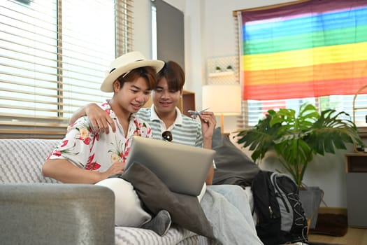 Excited young male lovers packing suitcase and booking hotel reservation via laptop at home.