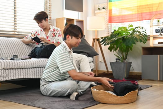 Young male lovers preparing for their new journey, packing suitcase in living room.