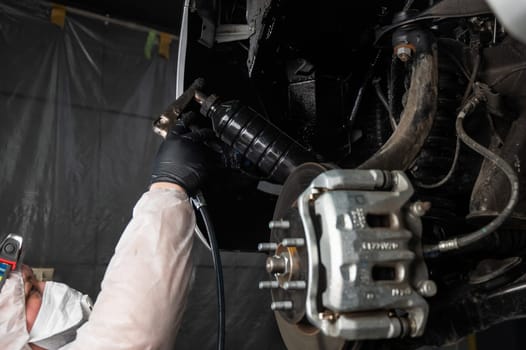 An auto mechanic applies anti-corrosion mastic to the underbody of a car