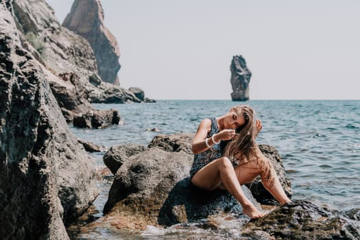 Woman travel sea. Young Happy woman in a long red dress posing on a beach near the sea on background of volcanic rocks, like in Iceland, sharing travel adventure journey