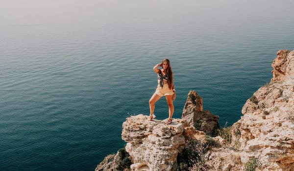 Woman travel sea. Happy tourist taking picture outdoors for memories. Woman traveler looks at the edge of the cliff on the sea bay of mountains, sharing travel adventure journey.