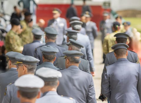 A group of men in military uniforms are lined up and walking down a street. Scene is serious and disciplined, as the men are dressed in their uniforms and appear to be following orders