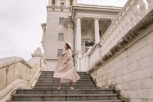 A woman in a hat stands on a set of stairs in front of a building. She is wearing a coat and a skirt