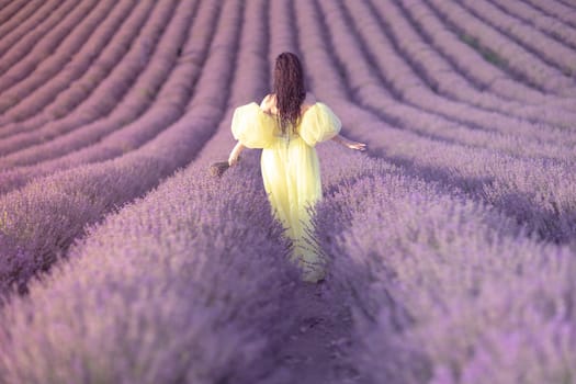 A woman in a yellow dress walks through a field of lavender. The field is full of purple flowers, and the woman is enjoying the scenery