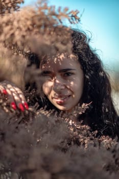 A woman is standing in a field of brown leaves. She is looking at the camera with a serious expression