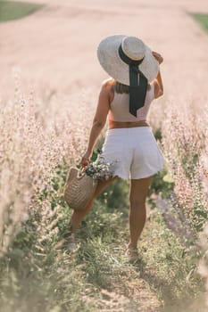 A woman wearing a straw hat and white shorts is walking through a field of flowers. She is holding a basket and a bouquet of flowers