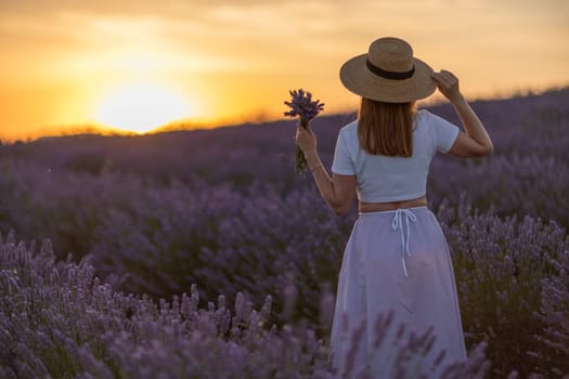 A woman stands in a field of lavender flowers, holding a bouquet of flowers. The sun is setting in the background, casting a warm glow over the scene. The woman's hat and dress add to the peaceful