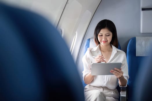 Businesswoman working on tablet during flight. Concept of business travel and digital connectivity.