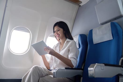 Businesswoman using tablet on airplane. Concept of business travel and digital connectivity.