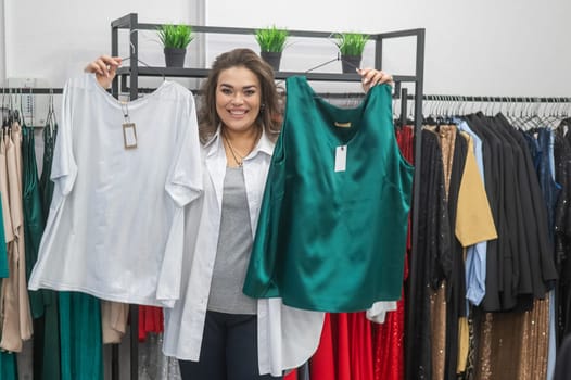 A fat woman chooses clothes by comparing them in a plus size store