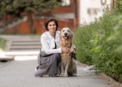Young Woman Poses Sitting With Golden Retriever On Street In Summer