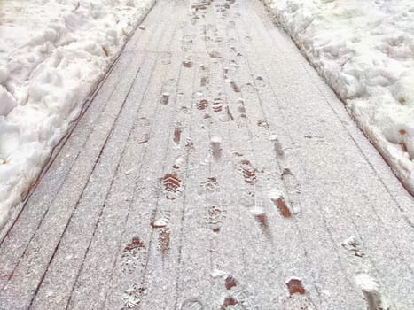 A snowy path is covered in multiple footprints, showcasing well-trodden route on a cold winter day