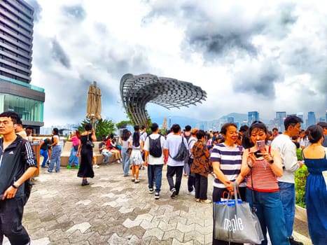 Hong Kong - April 05, 2024: People gather on the Hong Kong waterfront, with skyscrapers and Victoria Bay in the background on a cloudy afternoon