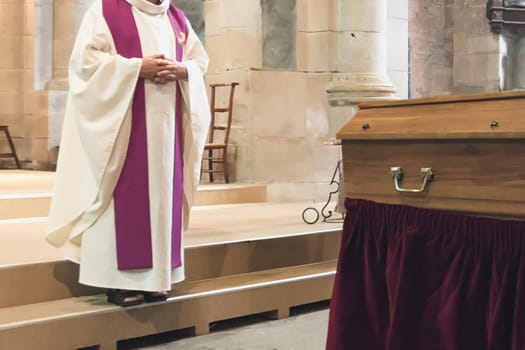 A priest in a church cassock conducts a funeral service in a French Catholic church