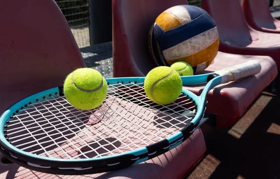 a tennis racket, balls and a volleyball on a bench on the sports tribune. High quality photo