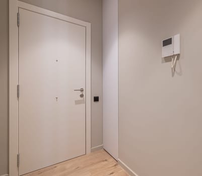 Minimalist hallway interior featuring a contemporary front door and intercom system. Clean lines and neutral colors enhance the modern aesthetic.