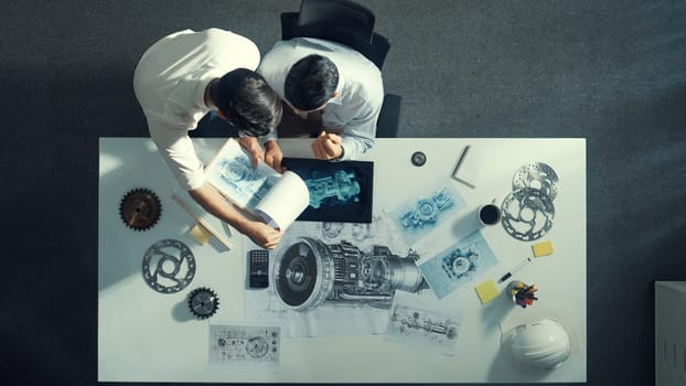 Top down aerial view of manager sitting while answer question about jet engine. Professional engineer looking at turbine engine or electronic generator while colleague asking question. Alimentation.