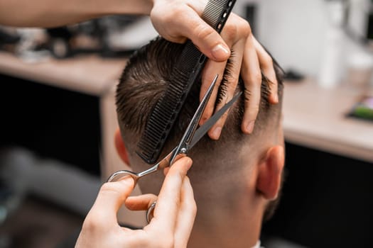 Barber uses scissors and a comb to cut the hair on the back of a man's head in a barbershop.