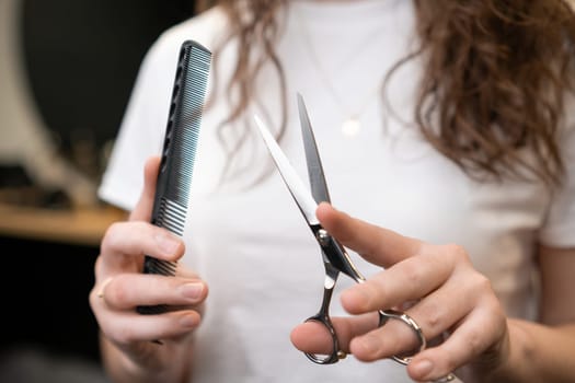 Hairdresser holding a comb and scissors in her hands standing in the salon.