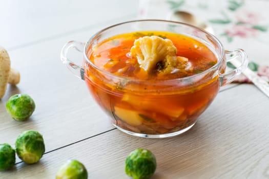 vegetable soup with Brussels sprouts and cauliflower, in a glass plate on a wooden table .