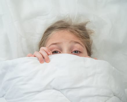 Top view of a little girl hiding under a blanket