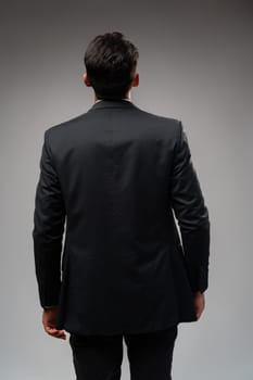 Young businessman from the back standing on gray background in studio