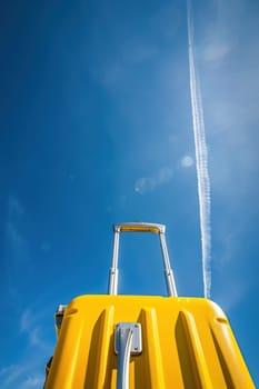 Travel in style vibrant yellow suitcase with contrail in blue sky illustrating wanderlust and adventure concept