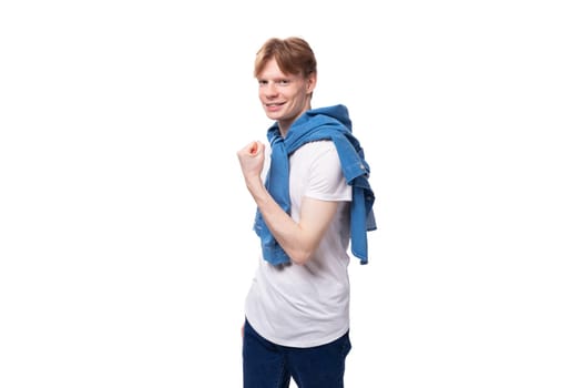 young well-groomed cute caucasian male student with golden red hair with a tattoo on his arms is dressed in a white t-shirt.