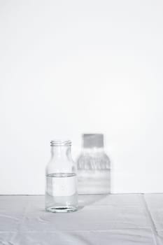 Empty transparent Glass Water bottle with shadow on white table and background with hard light, concept of pure still water