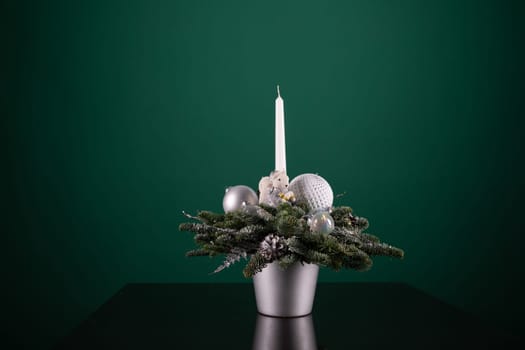 A silver vase containing a variety of Christmas decorations such as baubles, ribbons, and ornaments, alongside a white candle burning brightly. The scene is festive and adds a touch of holiday cheer to any room.