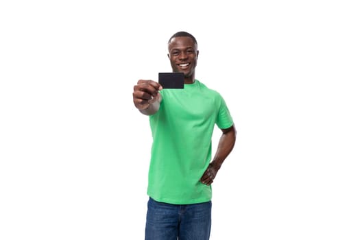 young surprised american man dressed in a green t-shirt and jeans advertises a credit card.