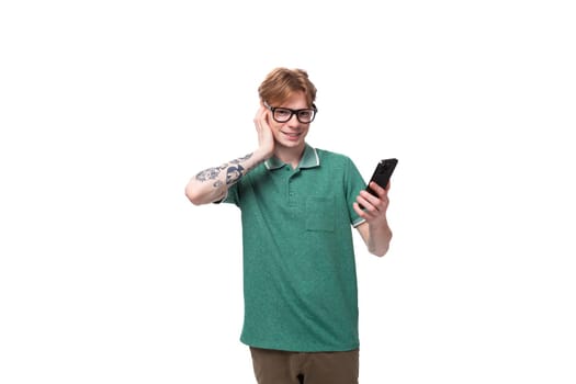 portrait of a young red-haired guy in a green t-shirt thoughtfully reading messages on a smartphone.