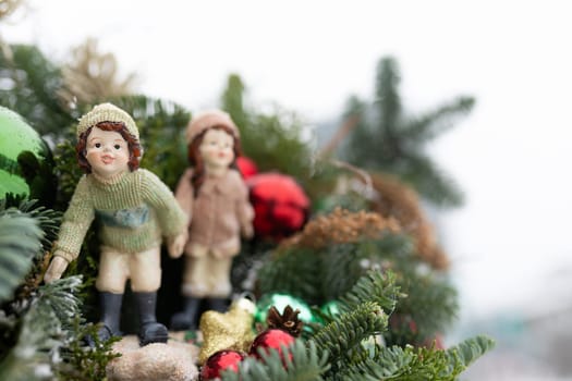 Two small figurines, resembling a man and a woman, are positioned on the peak of a Christmas tree. The man figurine wears a hat and a coat, while the woman figurine wears a dress. They are holding hands and appear to be in a joyful and festive pose.
