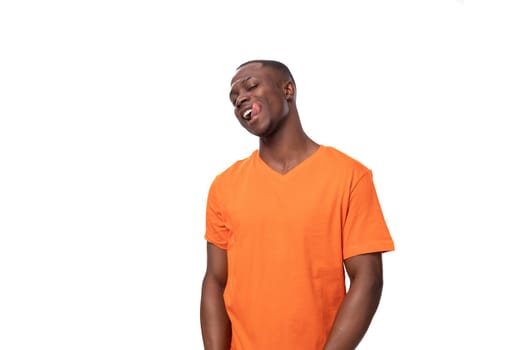 young modest handsome african man with short haircut wearing orange t-shirt smiling on white background with copy space.