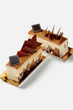 Two slices of delicate dessert with creamy caramel mousse, crunchy chocolate streusel and spiced poached pears, topped with soft caramel and chocolate decor on white background