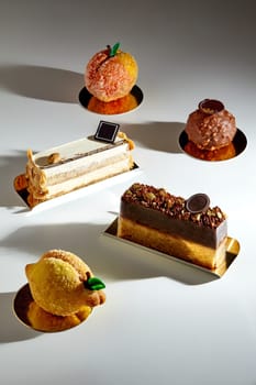 Variety of handcrafted desserts, velvety mousse and sponge layered cakes, crispy shortcrust pastries dusted with sugar in shape of fruits and chocolate praline truffle spotlighted on light surface