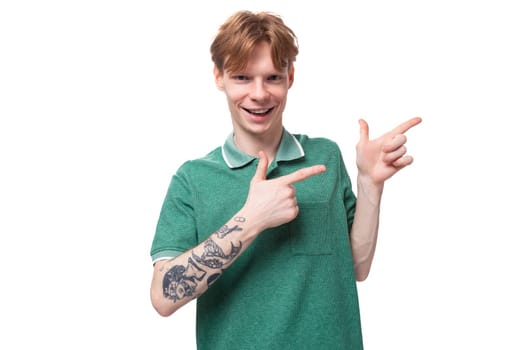 a young european man with red hair and a stylish hairstyle is dressed in a summer green t-shirt points his fingers towards the advertisement.