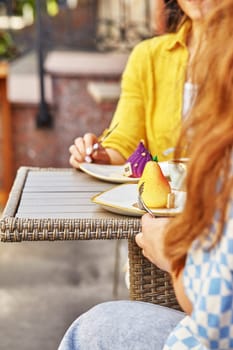 Two women savoring creative colorful desserts pear and fig shaped with coffee at cozy outdoor cafe setting, cropped shot