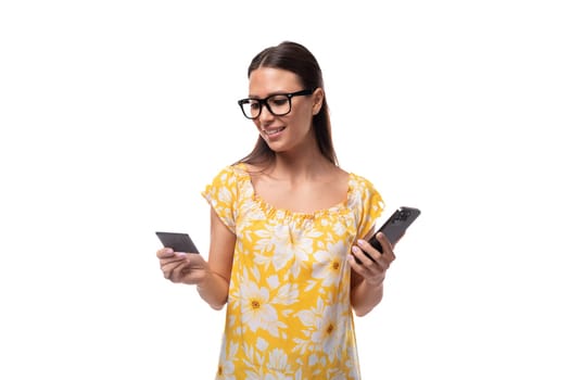 young brunette woman with straight hair dressed in a casual yellow T-shirt looks at the bank card data in her hands to use banking on her phone.