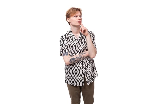 young focused caucasian man with red hair with a tattoo dressed in a summer black and white shirt on a background with copy space.