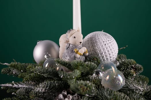 A white candle is placed on the very top of a decorated Christmas tree, symbolizing light and warmth during the holiday season. The candle stands out against the green branches and colorful ornaments.