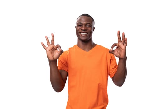 young african man dressed in orange t-shirt shows ok gesture and smiles.