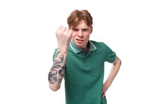 young caucasian man with red hair dressed in a green t-shirt shows his little finger on the background with copy space.