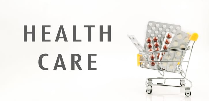 A cart full of medicine is labeled health care. The cart is silver and has a yellow handle