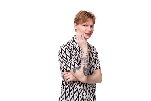 young positive caucasian man with red hair and a tattoo is dressed in a shirt with a rhombus pattern on a white background. people lifestyle concept.