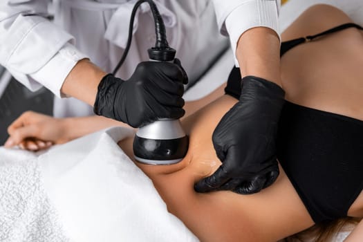 A cosmetologist utilizes an ultrasound device during a lifting procedure on a woman's abdomen