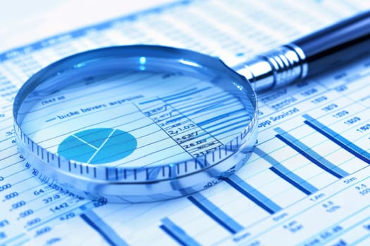 A magnifying glass is placed over financial data and charts, highlighting the importance of detailed analysis and scrutiny in the business and finance sectors